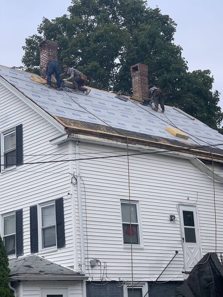 Crew installing new shingles on a white colonial