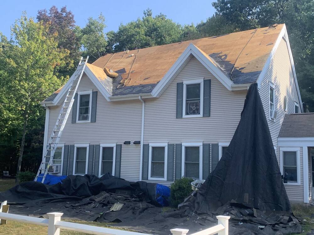 Cape with two front dormers stripped to the roof deck, yard protected with tarps